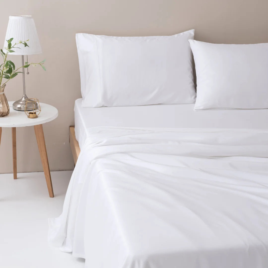 Neat and clean bedroom setup with Linenly's ultra-soft white bamboo sheet set and a bedside table featuring a lamp and a vase with greenery.
