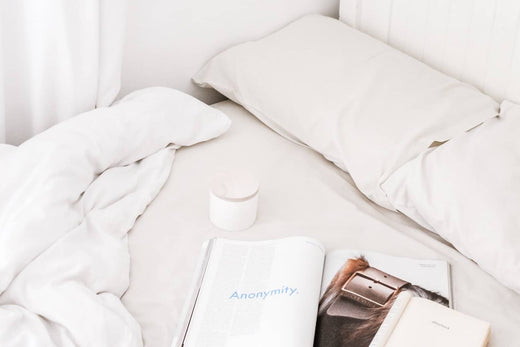 a container and a book in bed with white sheets and pillows