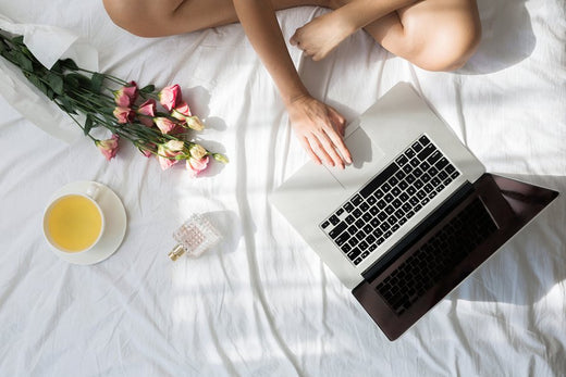 a person sitting in the bed with white bed sheet and flowers while working in a laptop