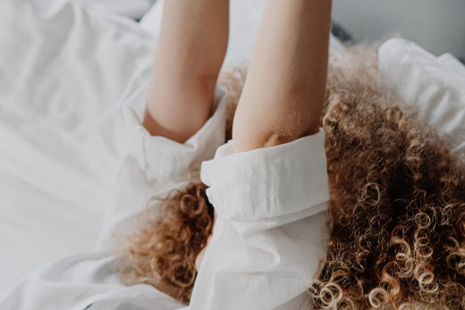 a woman lying in bed with white bed sheets while raising her hands