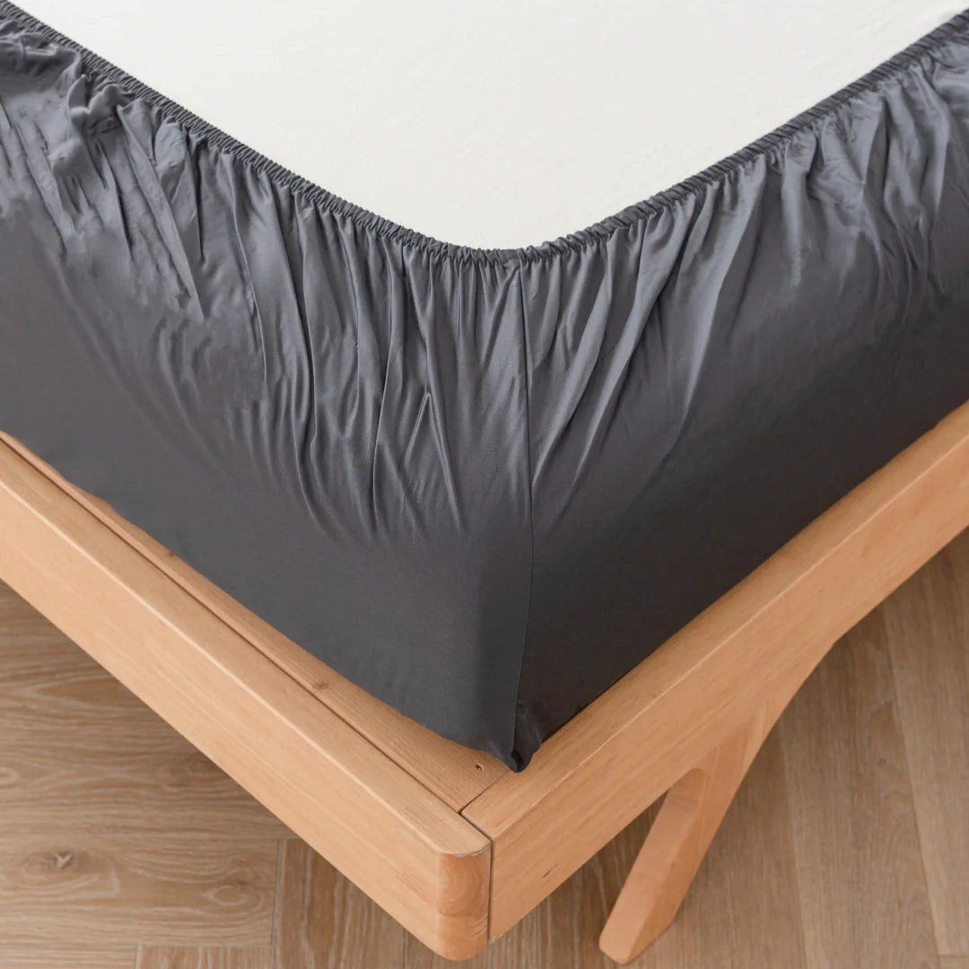 A neatly fitted Linenly Bamboo Fitted Sheet in Charcoal on a wooden bed frame, emphasizing the corner detail where the sheet tucks under the mattress.