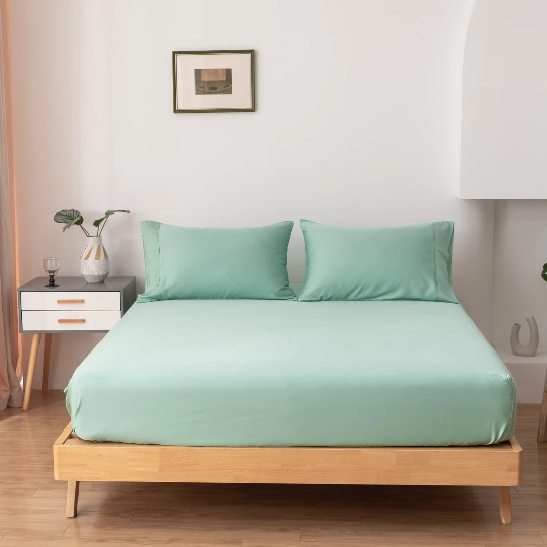 A neatly made bed with Linenly's green Bamboo Fitted Sheet in a minimalist bedroom, accompanied by a nightstand and decorative items, creating a serene and cozy atmosphere.