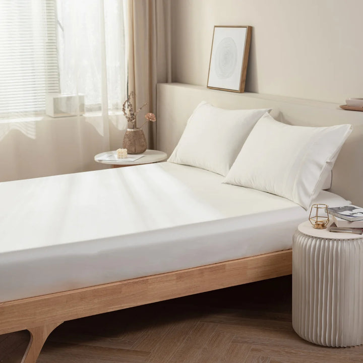 A minimalist bedroom with neatly made bed, crisp Linenly Ivory Bamboo Fitted Sheets, a wooden bed frame, and simple decor creating a serene and uncluttered space.