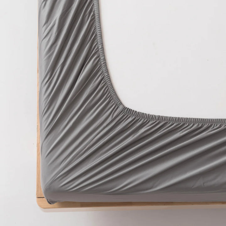 Close-up of a neatly fitted Linenly Stone Grey Bamboo Fitted Sheet on a wooden bed frame, showcasing the fabric's luxuriously soft texture and precise corner fitting.