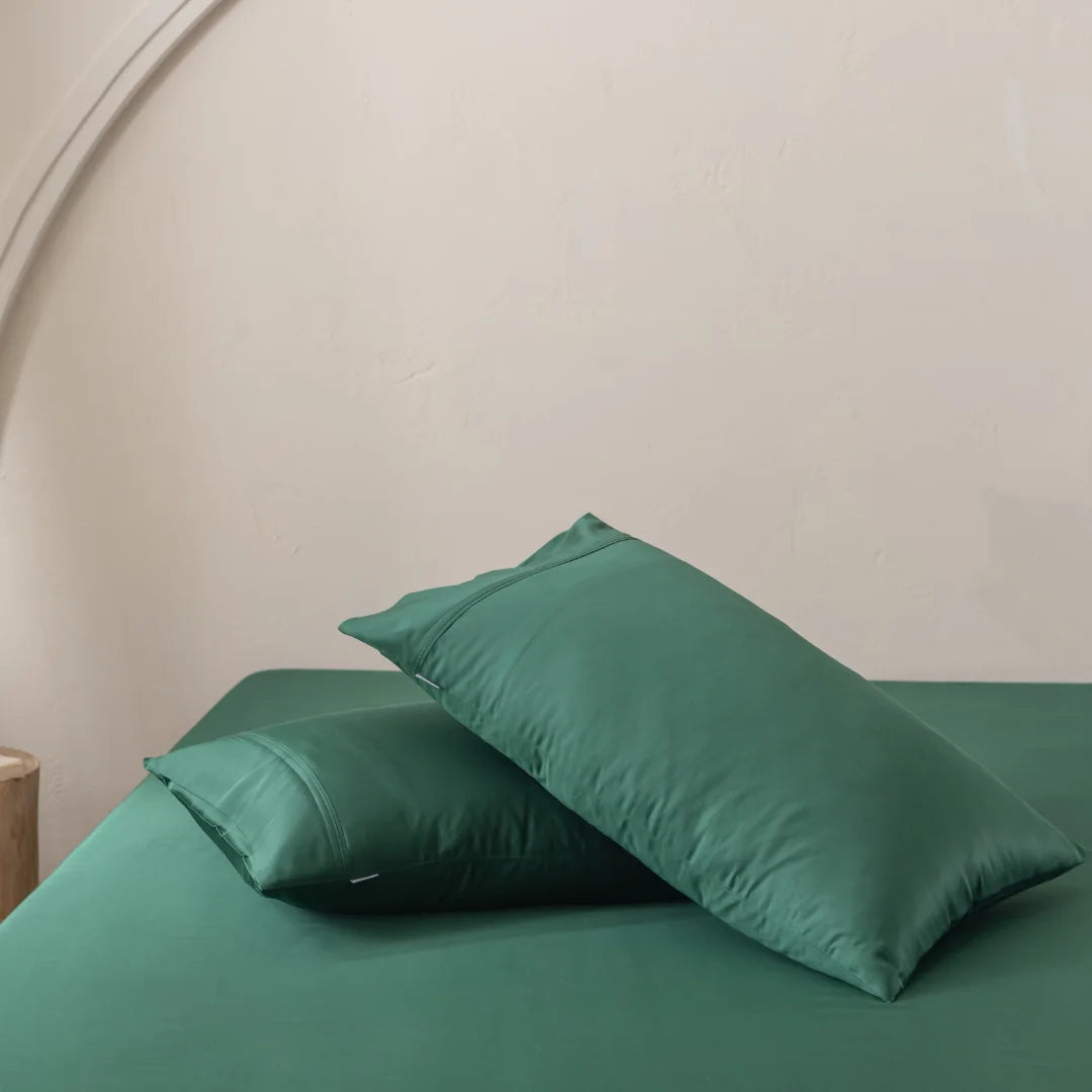 Two Linenly Bamboo Pillowcase Set - Evergreen pillows rest on a bed adorned with organic bamboo bedding, set against a light-colored wall with an arched structure, creating a serene and cozy atmosphere.