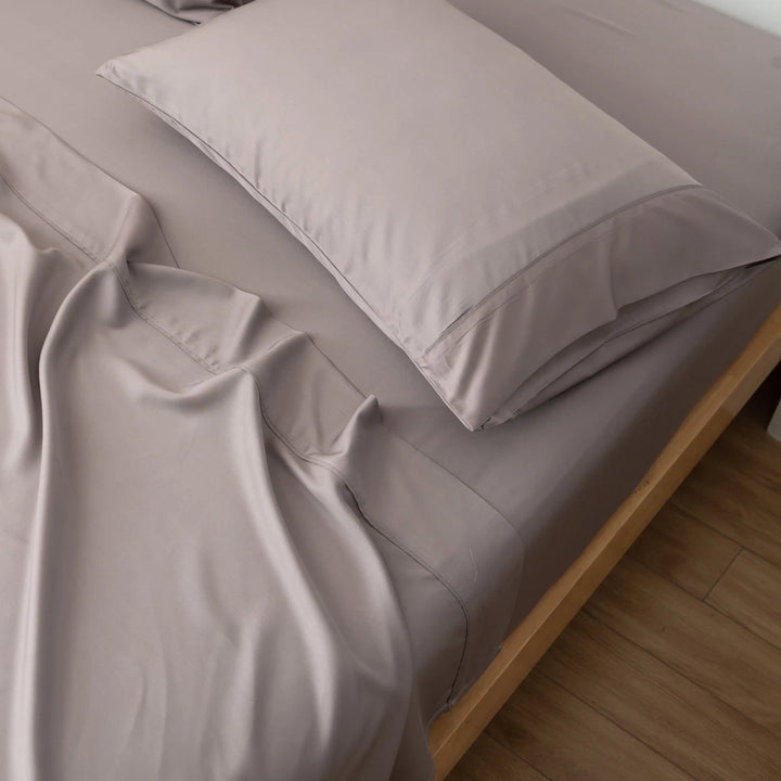 An unmade bed with crumpled gray sheets and a Linenly Bamboo Pillowcase Set in Stone Terrace, suggesting a recent awakening or a pause in tidying up.