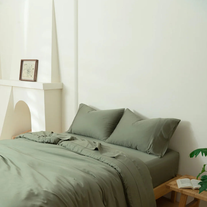 A neatly made bed with environmentally friendly Linenly Bamboo Quilt Cover in a serene, minimalist bedroom with a touch of greenery.