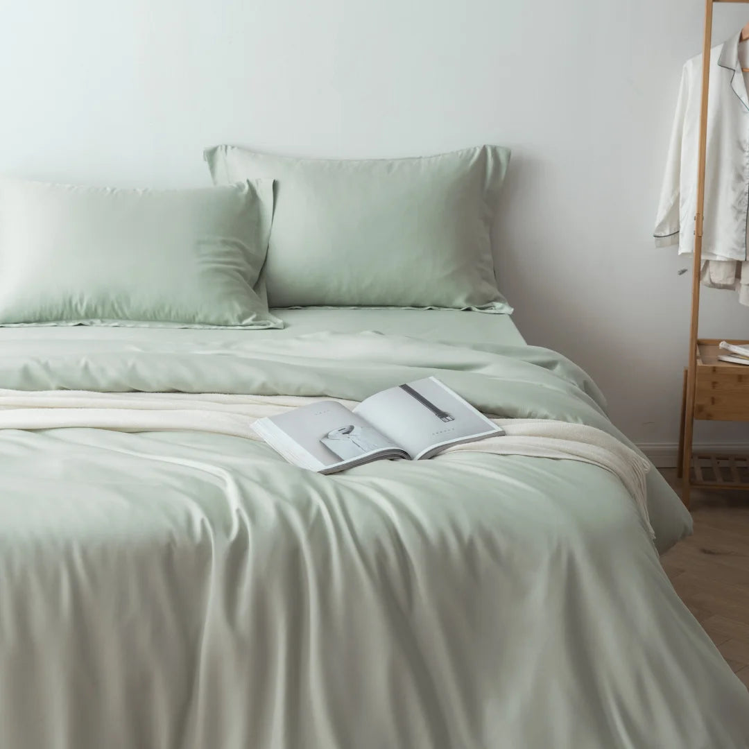 A serene bedroom scene featuring a neatly made bed with a Linenly soft sage bamboo quilt cover, complemented by an open book resting in the center, inviting a peaceful reading session.