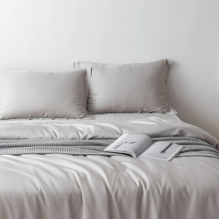 A tranquil and neatly made bed with luxurious, soft grey Linenly Silver Bamboo Quilt Cover and an open book lying in the middle, inviting a peaceful reading session.