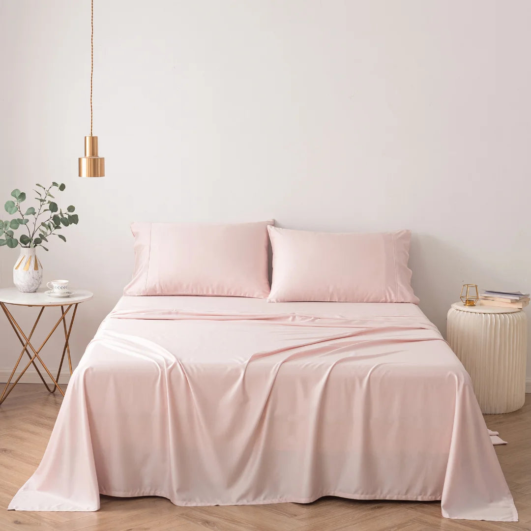 A serene bedroom corner featuring a neatly made bed outfitted in Linenly's ultra-soft Blush Bamboo Sheet Set, complemented by a simple white side table with a plant, and a chic hanging pendant light.