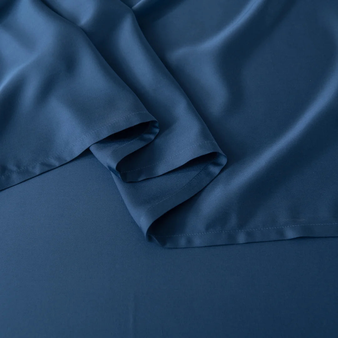 The Bamboo Sheet Set - Midnight from Linenly is crafted from a silky-smooth, deep blue satin fabric that drapes elegantly over any surface, showcasing gentle folds and a soft sheen.