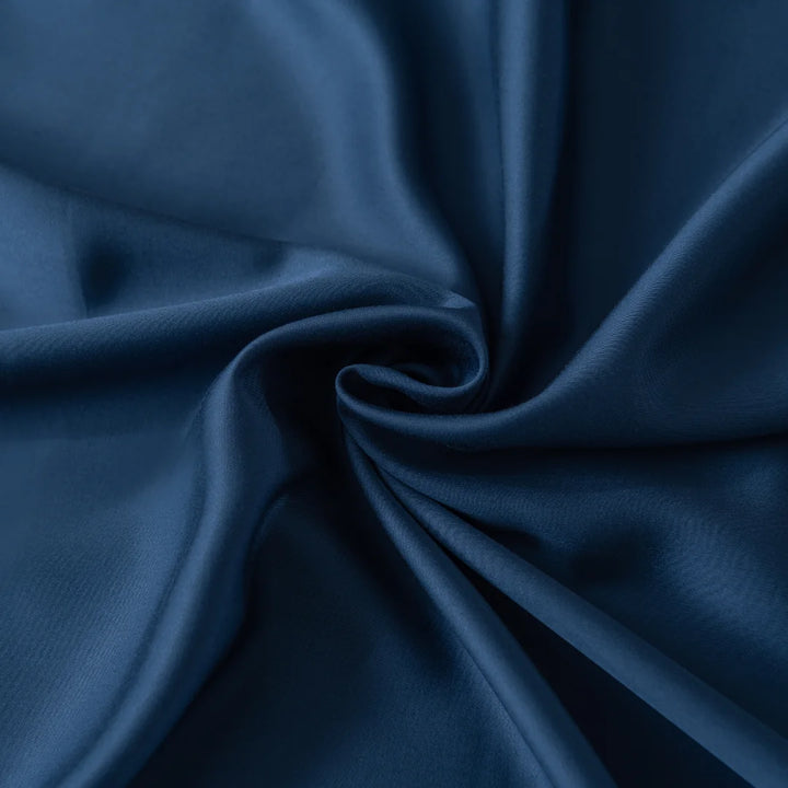 A close-up of the Bamboo Sheet Set - Midnight by Linenly shows dark blue fabric gathered in a spiral pattern. The silky texture and smooth folds reflect light, highlighting the ultra-soft material's shiny surface, reminiscent of luxurious sheets.