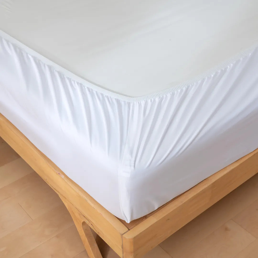 A close-up of the Linenly Luxe Cotton Sateen Fitted Sheet in white, neatly stretched over a wooden bed frame, highlights the sheet's corner and perfect fit for a touch of luxury.