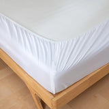 A close-up of the Linenly Luxe Cotton Sateen Fitted Sheet in white, neatly stretched over a wooden bed frame, highlights the sheet's corner and perfect fit for a touch of luxury.