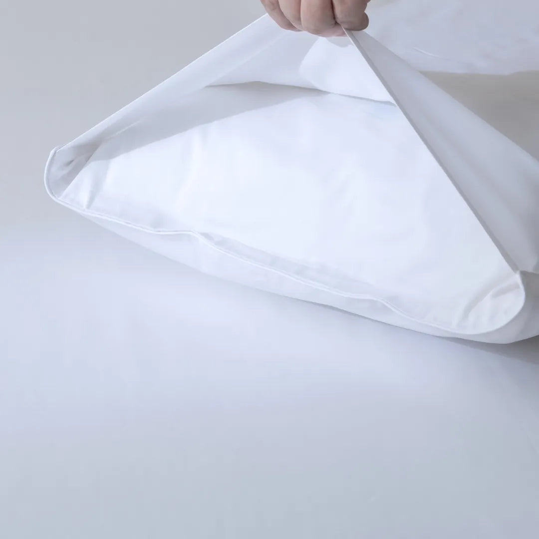A hand is placing a pillow into the Linenly Luxe Cotton Sateen Pillowcase Set in white, shown against a plain white background.