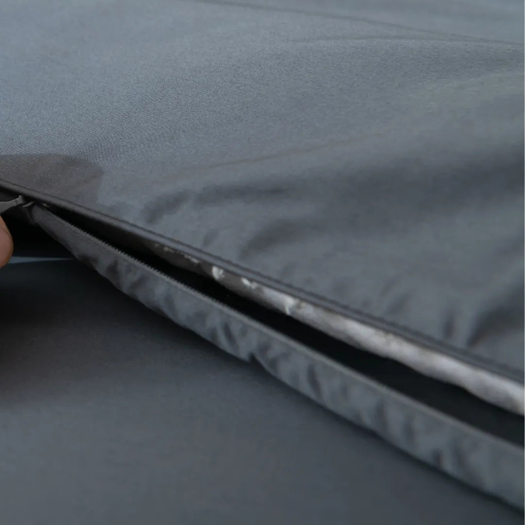A close-up of a hand unzipping the Luxe Cotton Sateen Quilt Cover - Charcoal by Linenly, revealing a white padded layer inside.