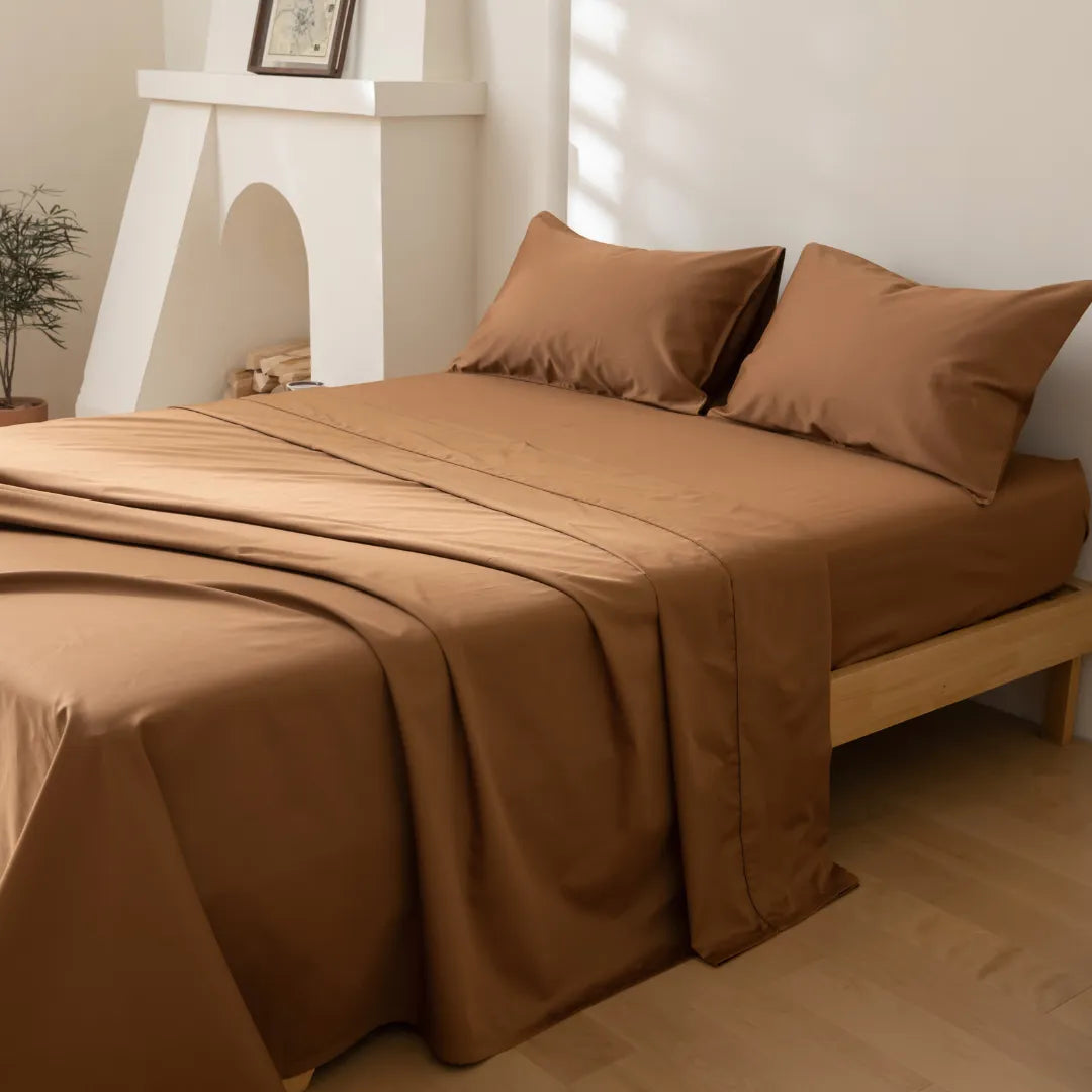 A neatly made bed with Linenly's Luxe Sateen Sheet Set in Terracotta cotton in a serene bedroom setting, featuring a minimalist fireplace mantel in the background.