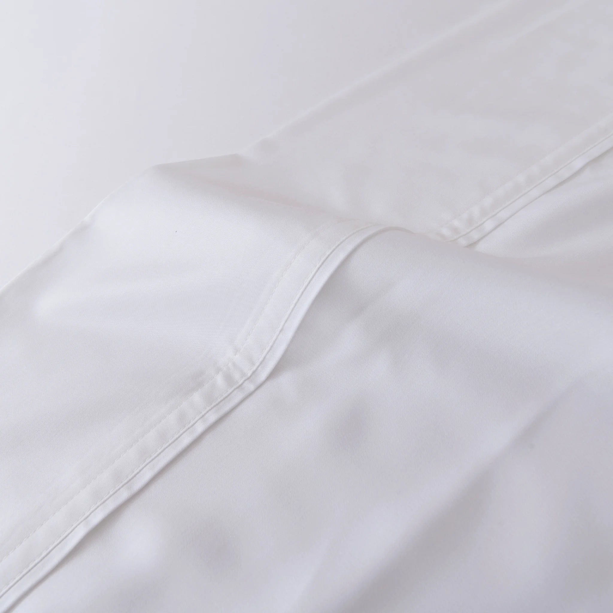 A close-up of the Linenly Bamboo Fitted Sheet - White, neatly folded to showcase its visible stitching, smooth fabric texture, and luxurious softness.