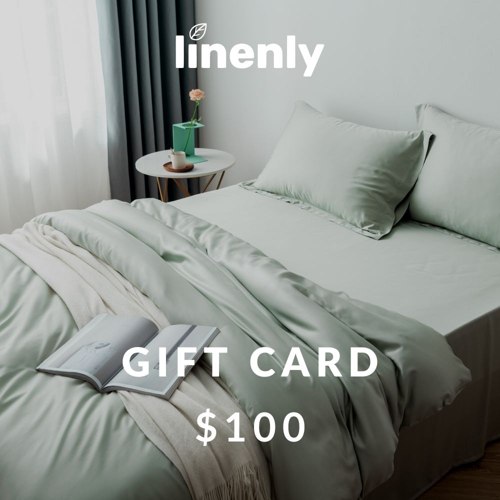 A neatly made bed with mint green sheets and pillows is shown. A white blanket and an open book rest on the bed, promising a good night's sleep. Next to the bed is a small white side table holding a potted plant. The text on the image reads "Linenly" and "Gift Cards $100".